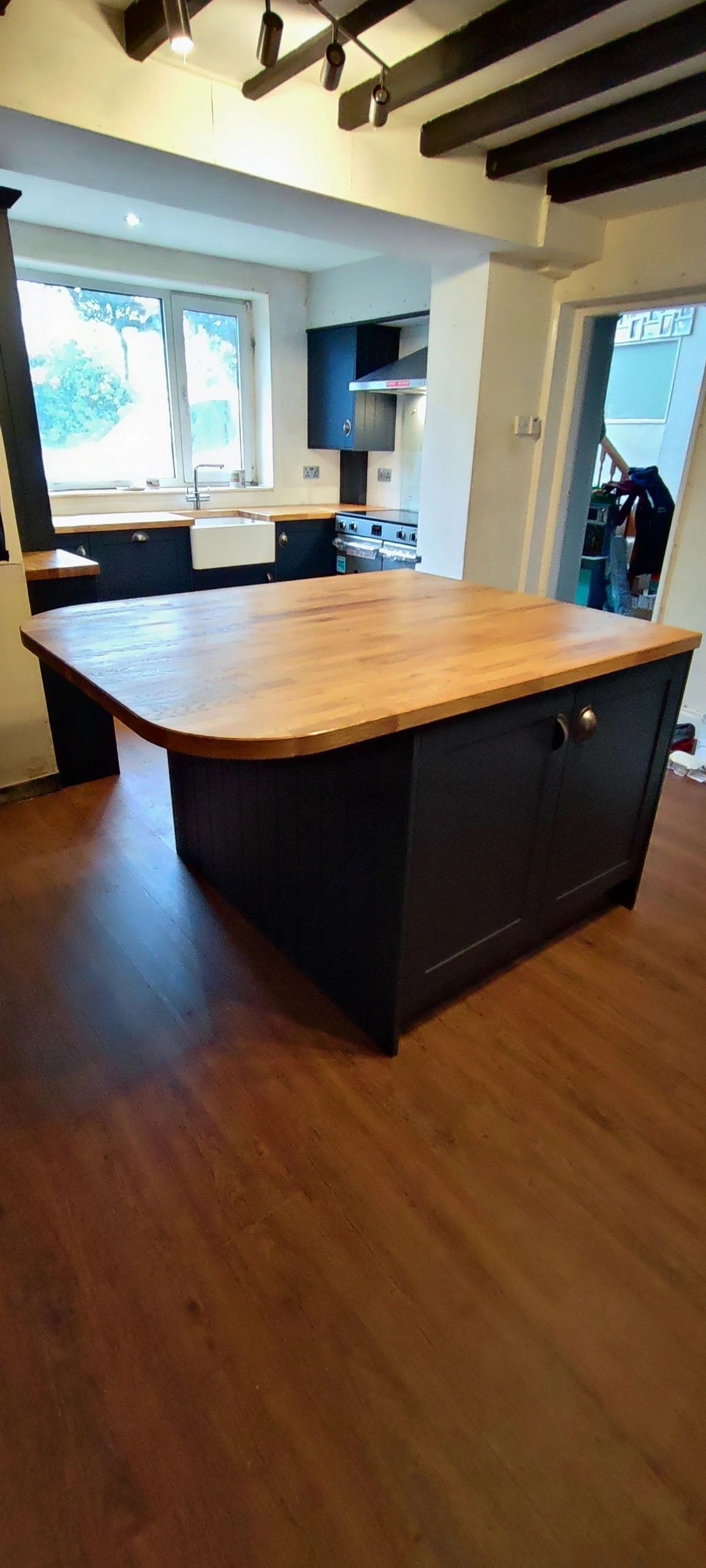 Navy kitchen island with an oak worktop beneath a beamed ceiling