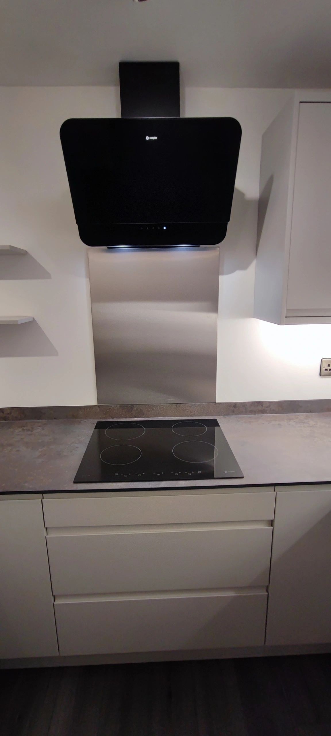 Induction hob with a stainless splashback and an angled black hood