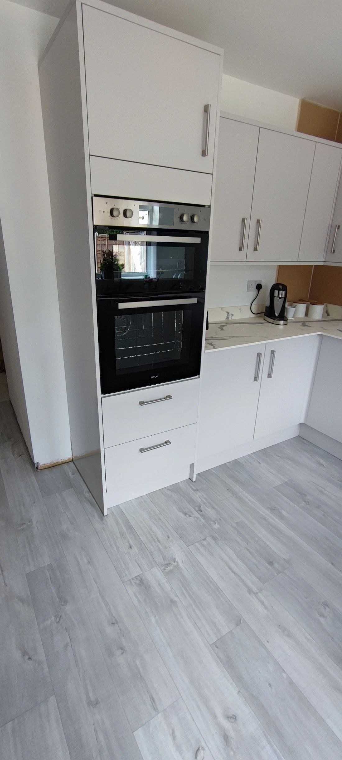 White kitchen with tall oven housing and grey wood-effect floor